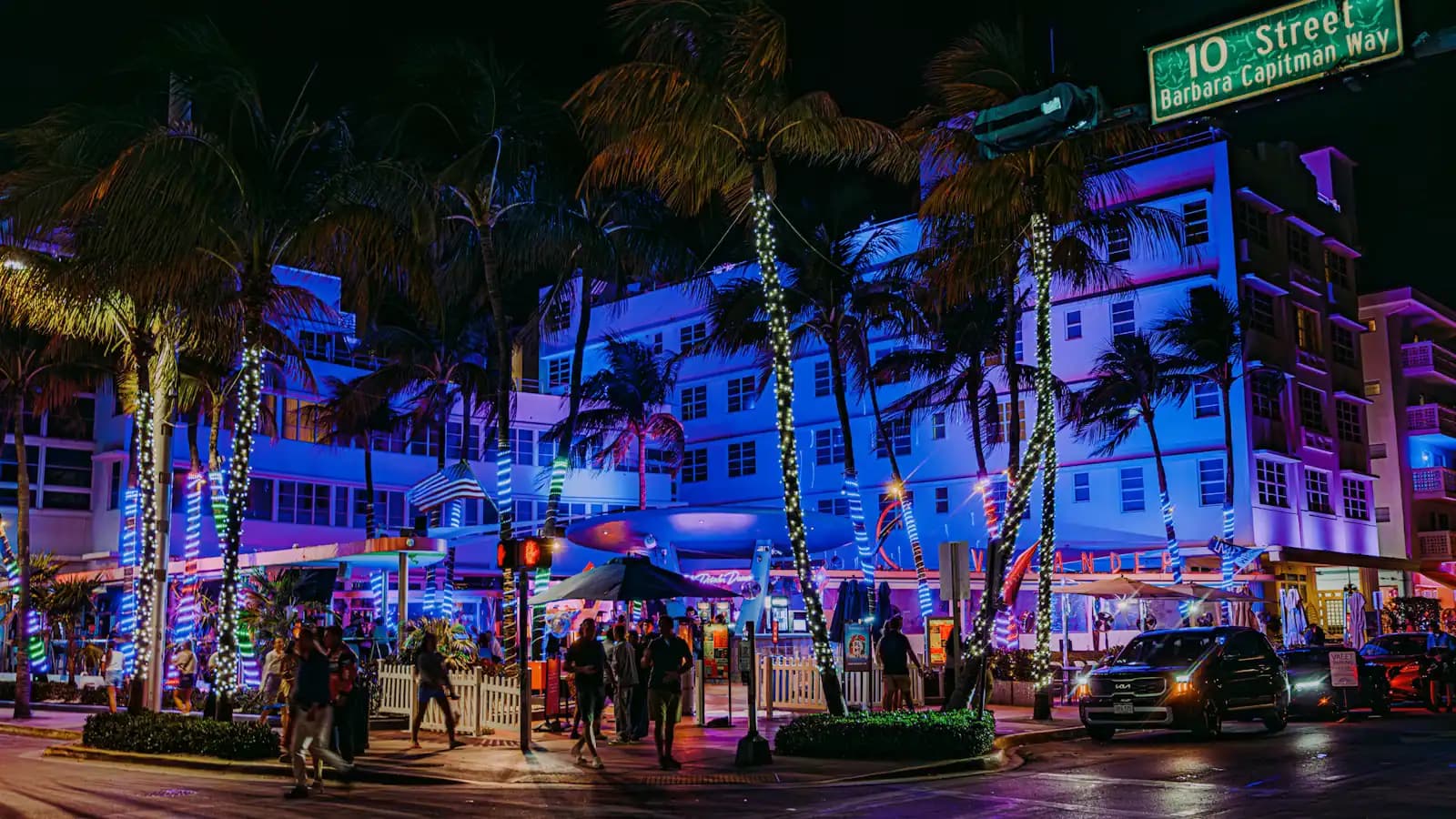 A city street after dark with neon-lit building frontages and palm trees along the kerb