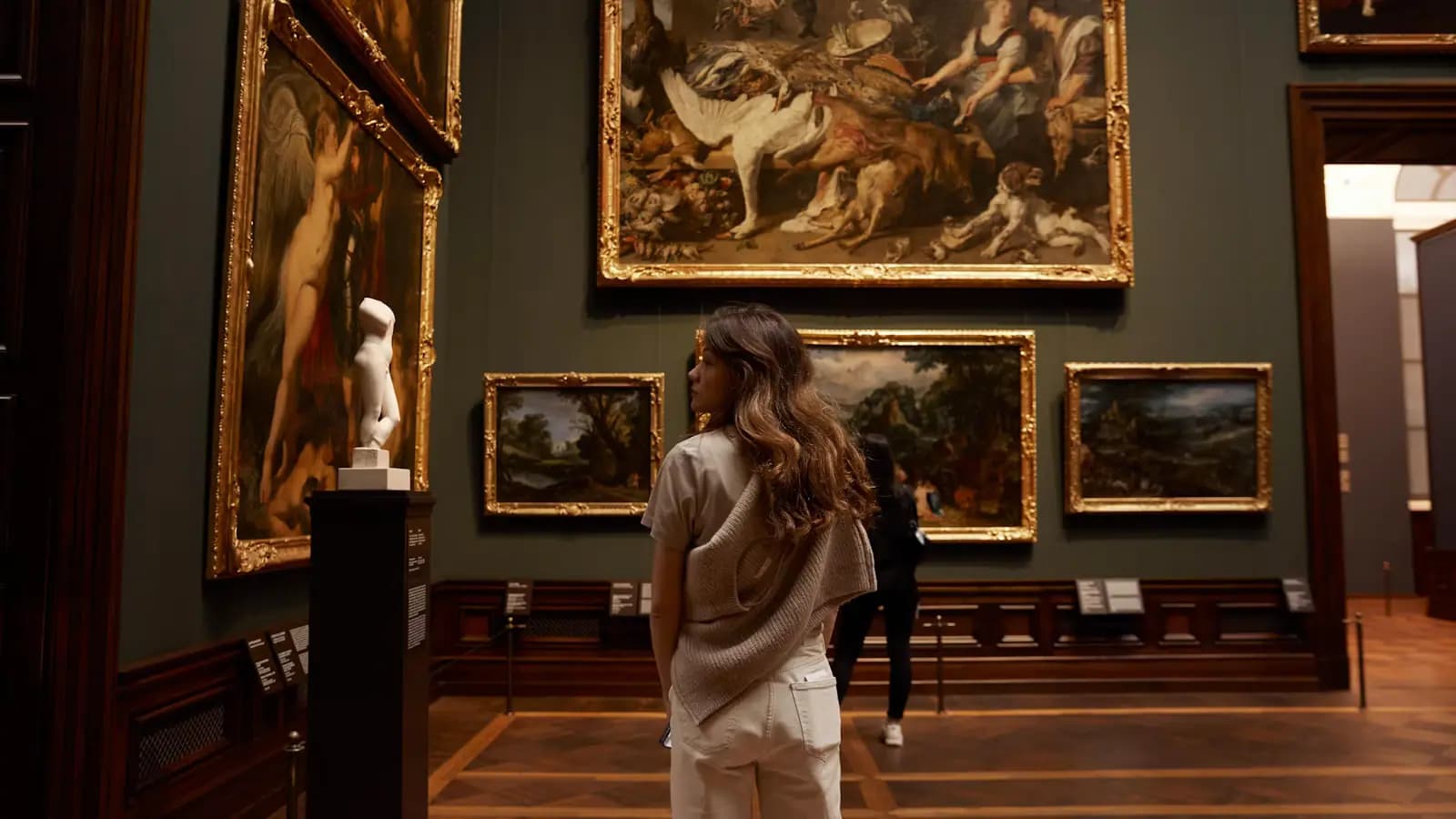A visitor standing in a gallery looking at paintings hung on a white wall