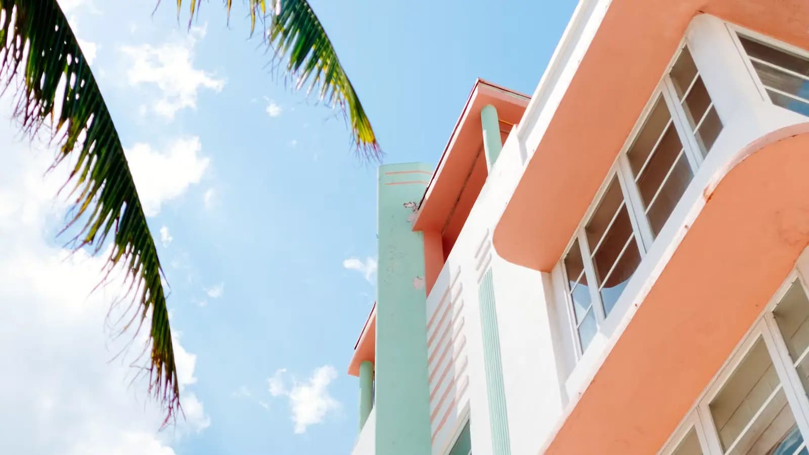 Peach and mint Art Deco facade in Miami Beach seen from below with a palm frond against a blue sky