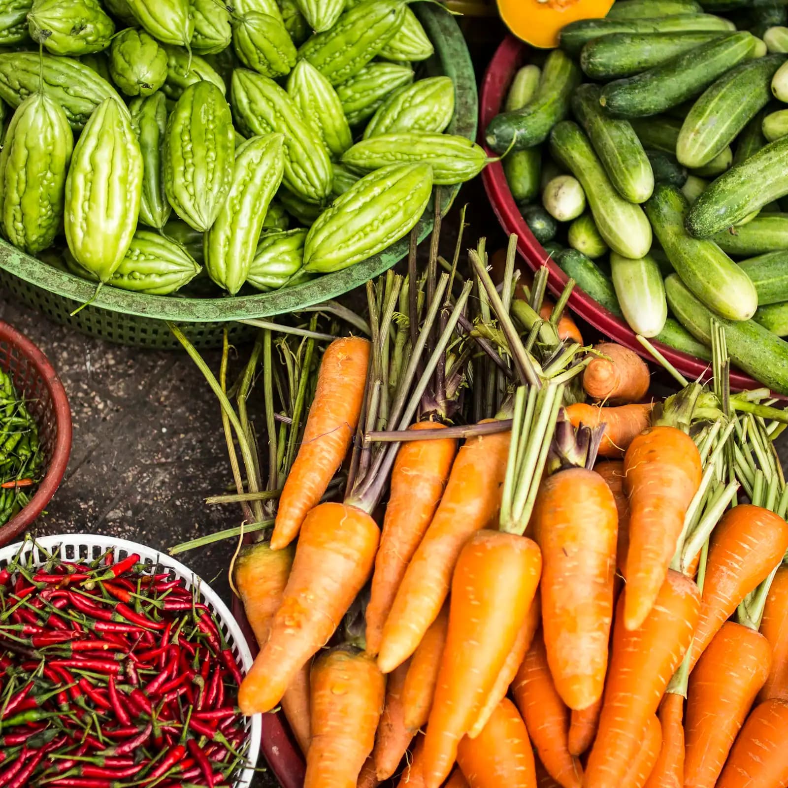 Baskets of fresh vegetables laid out on the ground at a market stall