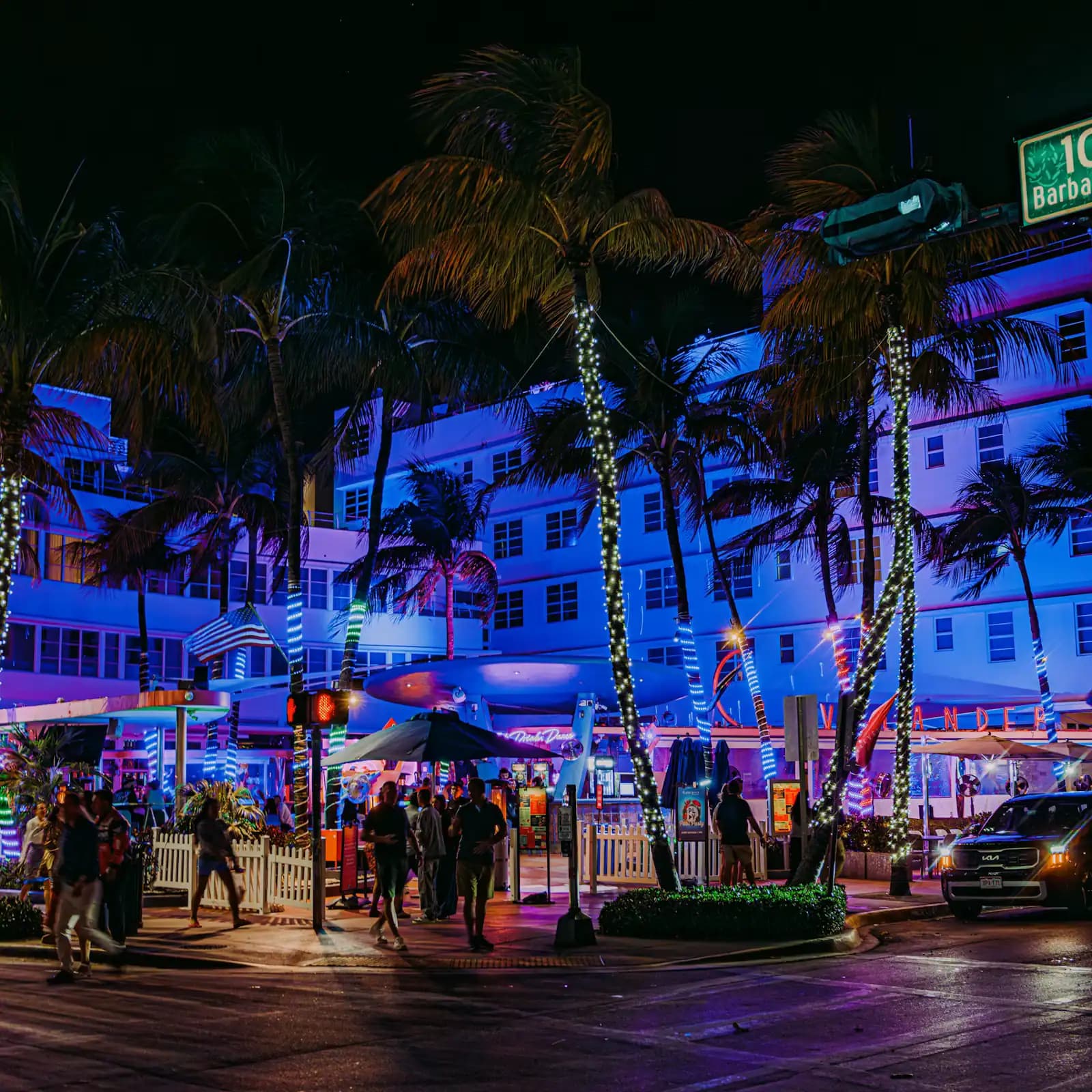A city street after dark with neon-lit building frontages and palm trees along the kerb