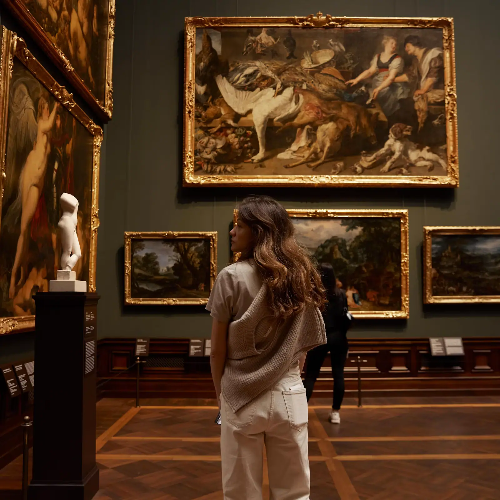 A visitor standing in a gallery looking at paintings hung on a white wall