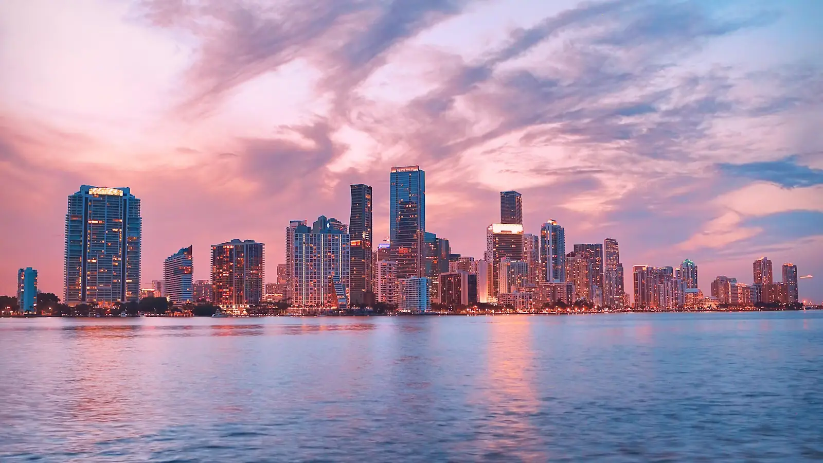 The Miami skyline at dusk seen across Biscayne Bay under a pink and violet sky